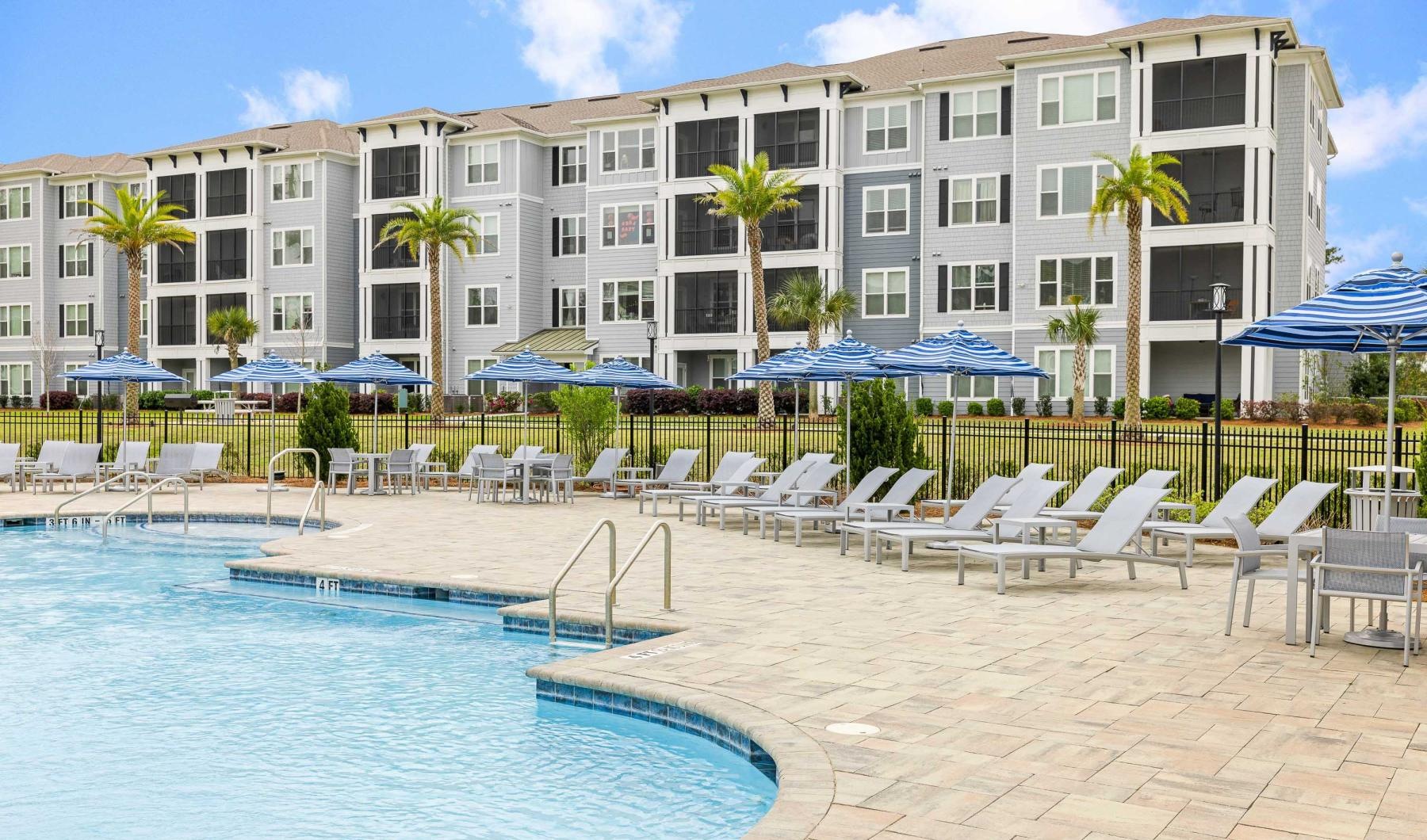 a pool with chairs and umbrellas by a building
